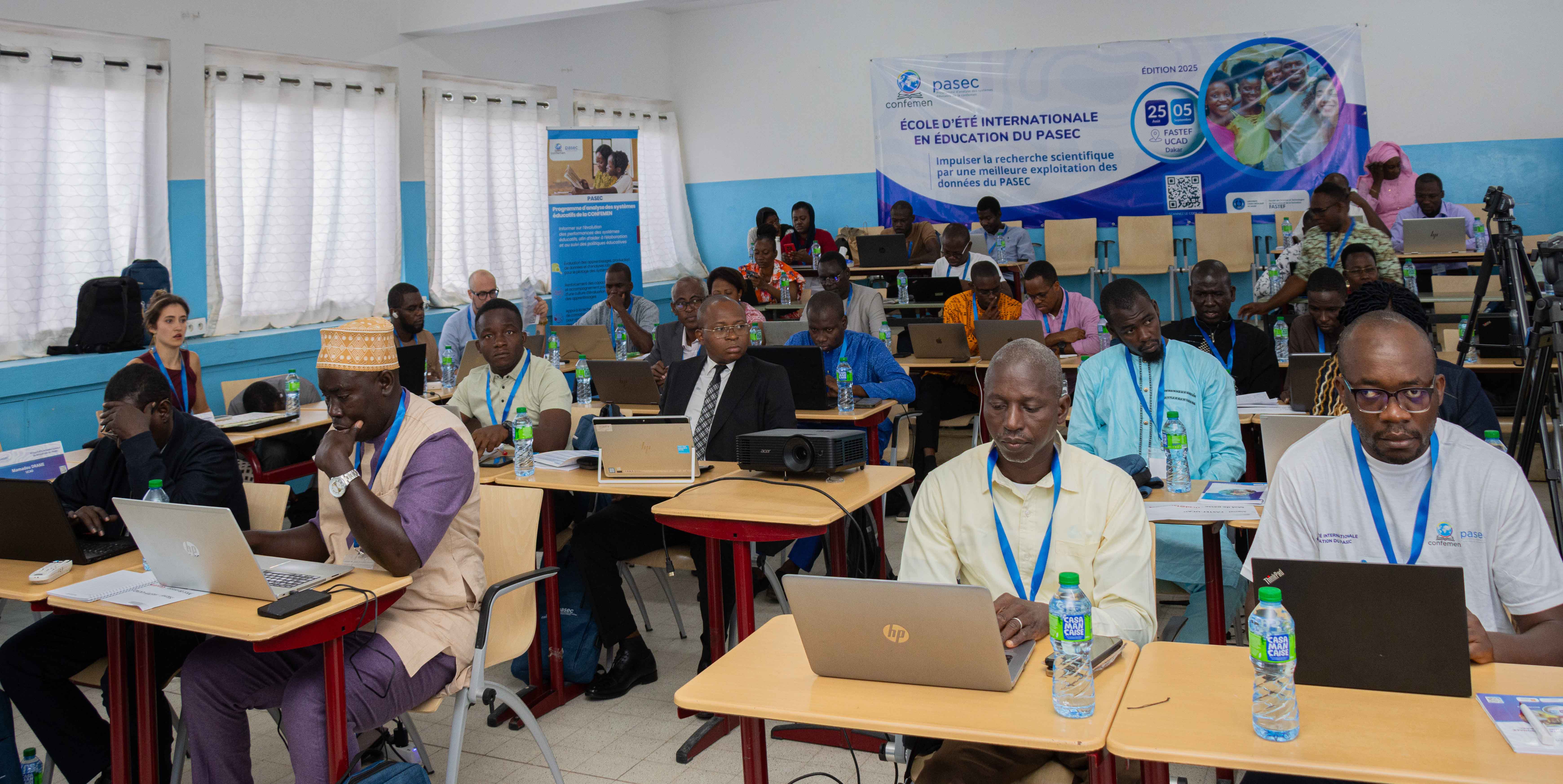 Participants de l'École d'Été PASEC 2025 en session de formation - Salle de classe avec ordinateurs portables et bannière PASEC